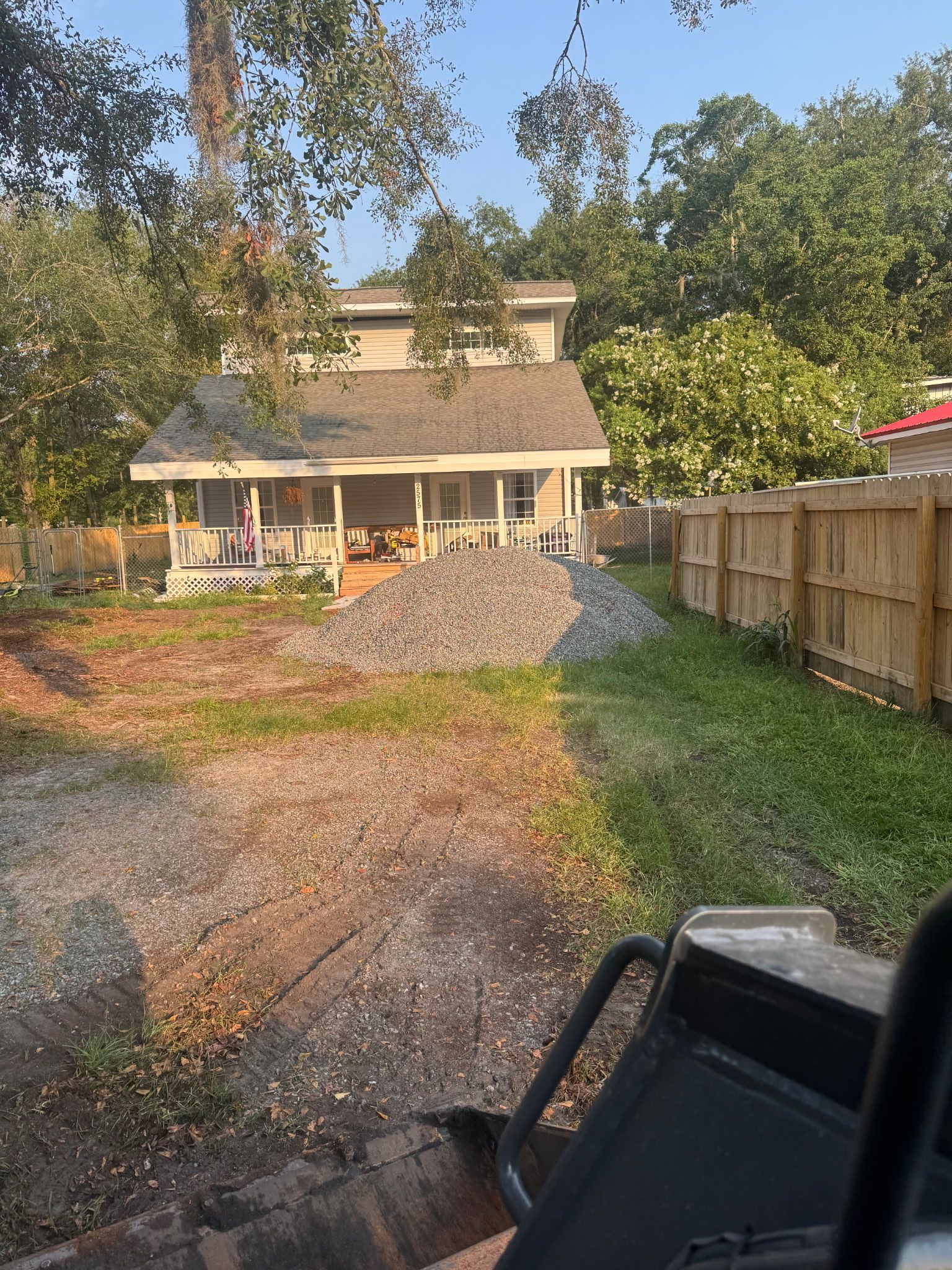 Gravel driveway leading to a porch house, with a wooden fence and trees in warm evening light