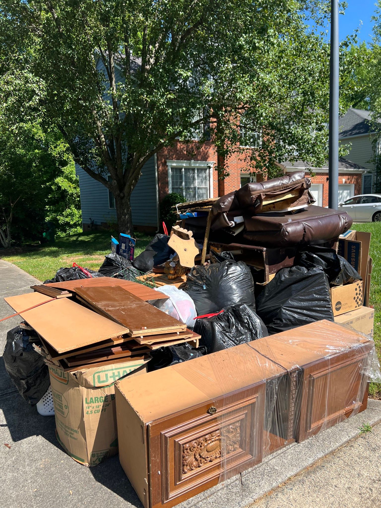 A pile of discarded furniture, cardboard boxes, and trash bags sitting on a curb in front of a house.