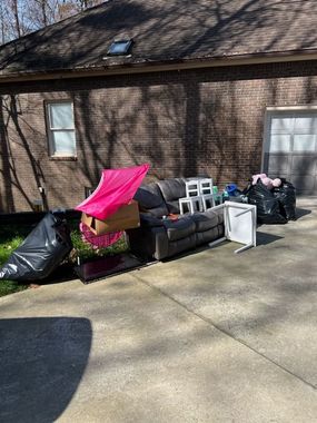A pile of discarded furniture, including a sofa, small table, and trash bags, on a residential concrete driveway.