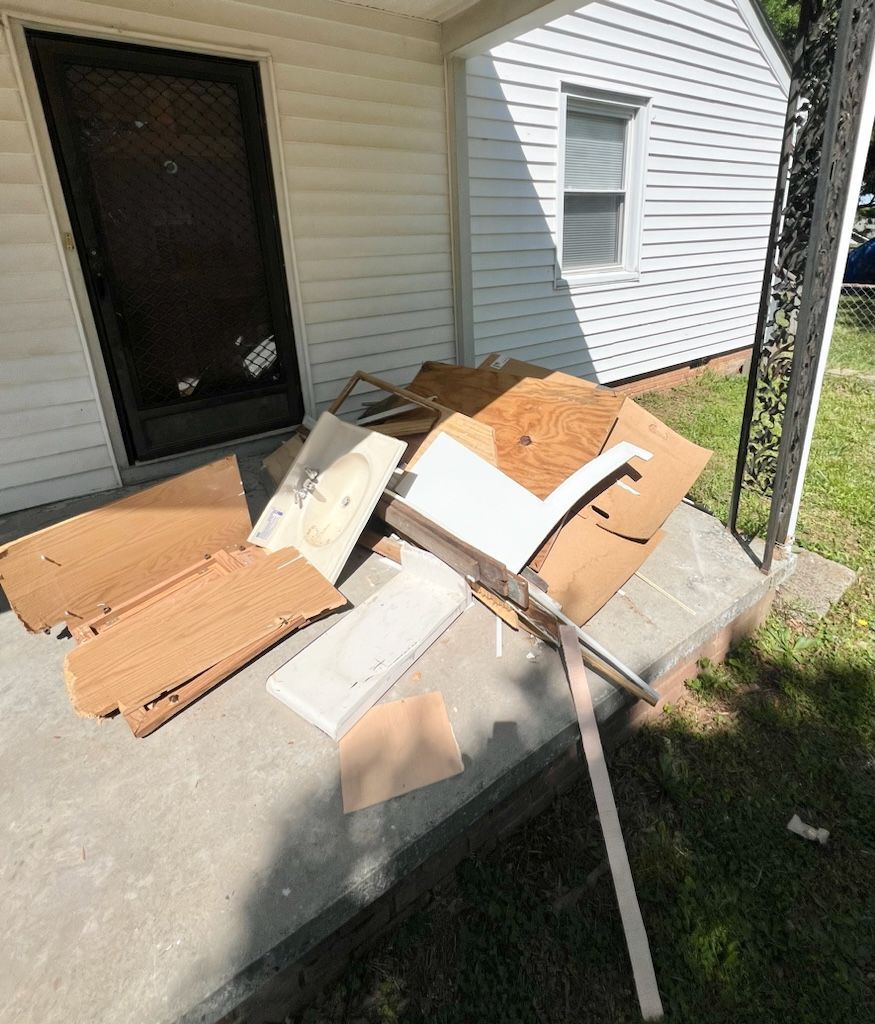 A pile of flattened cardboard boxes and white packing foam sits on a concrete porch in front of a white house.