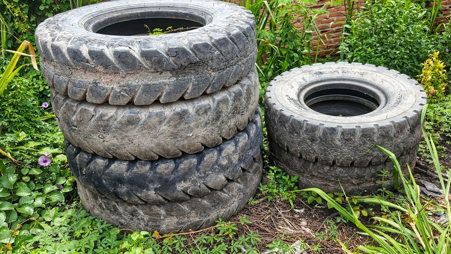 A stack of three weathered, dirty rubber tires beside a single tire in a grassy, outdoor area.