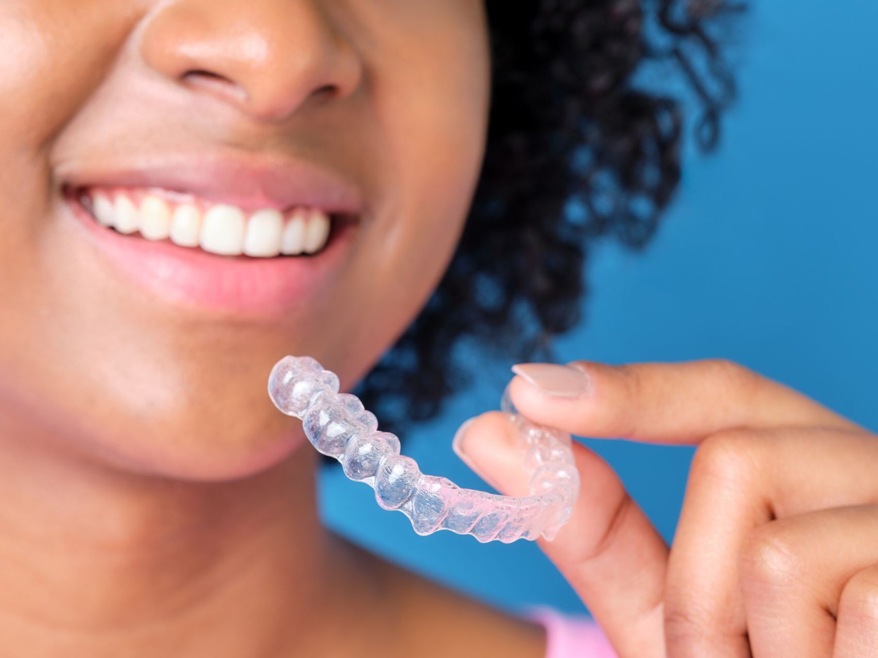 Get Invisalign Clear Aligners From Our Top Cosmetic Dentist in Somerset, NJ. woman smiling holding clear aligners | cosmetic dentist in somerset, NJ