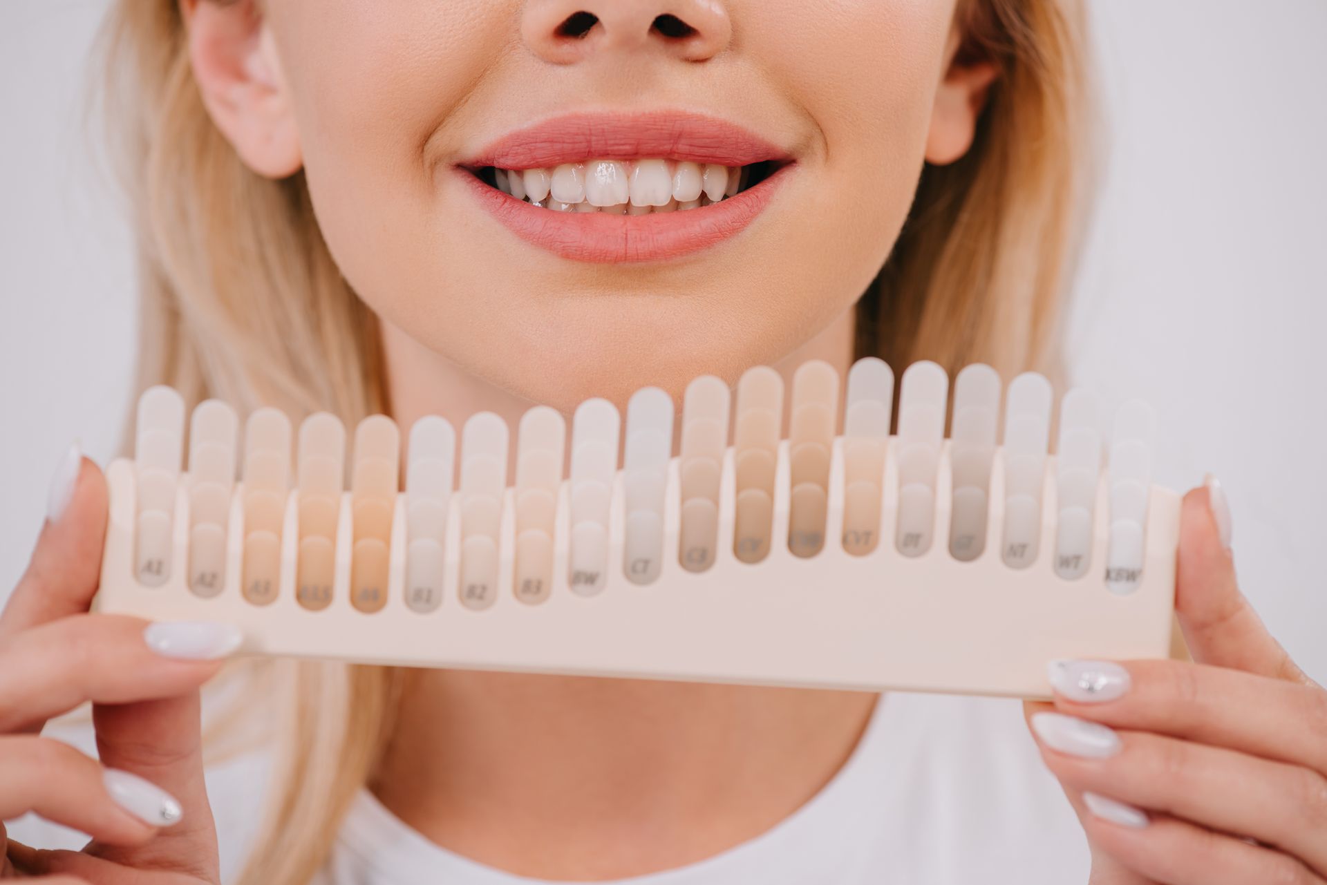 Get professional teeth whitening by our qualified cosmetic dentist in Somerset, NJ. woman holding different shades of teeth | teeth whitening by our top cosmetic dentist in Somerset, NJ