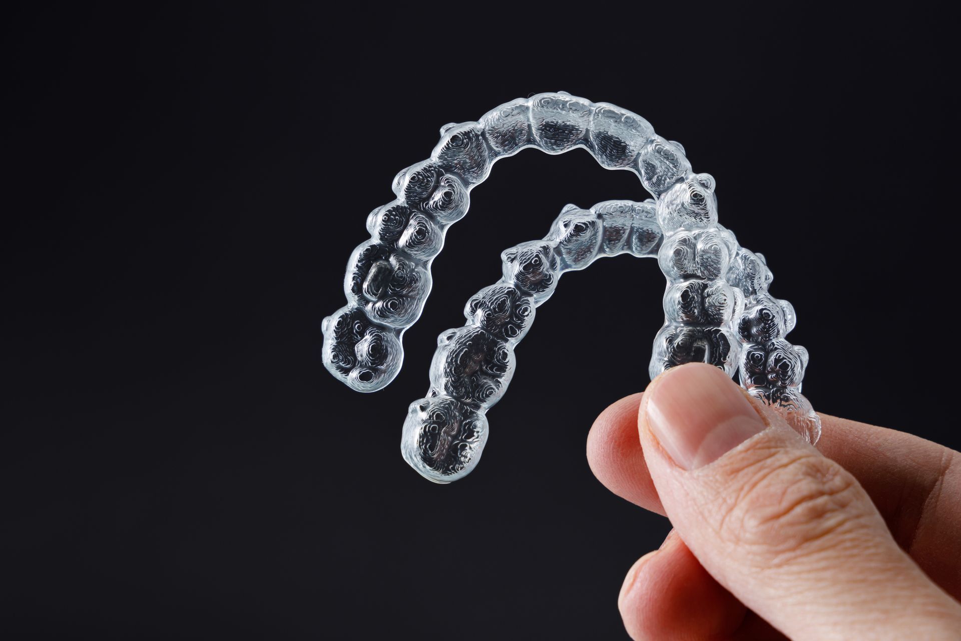 Get invisible braces in Somerset, NJ. holding clear aligners against black background | Affordable cosmetic Invisalign in Somerset, NJ.