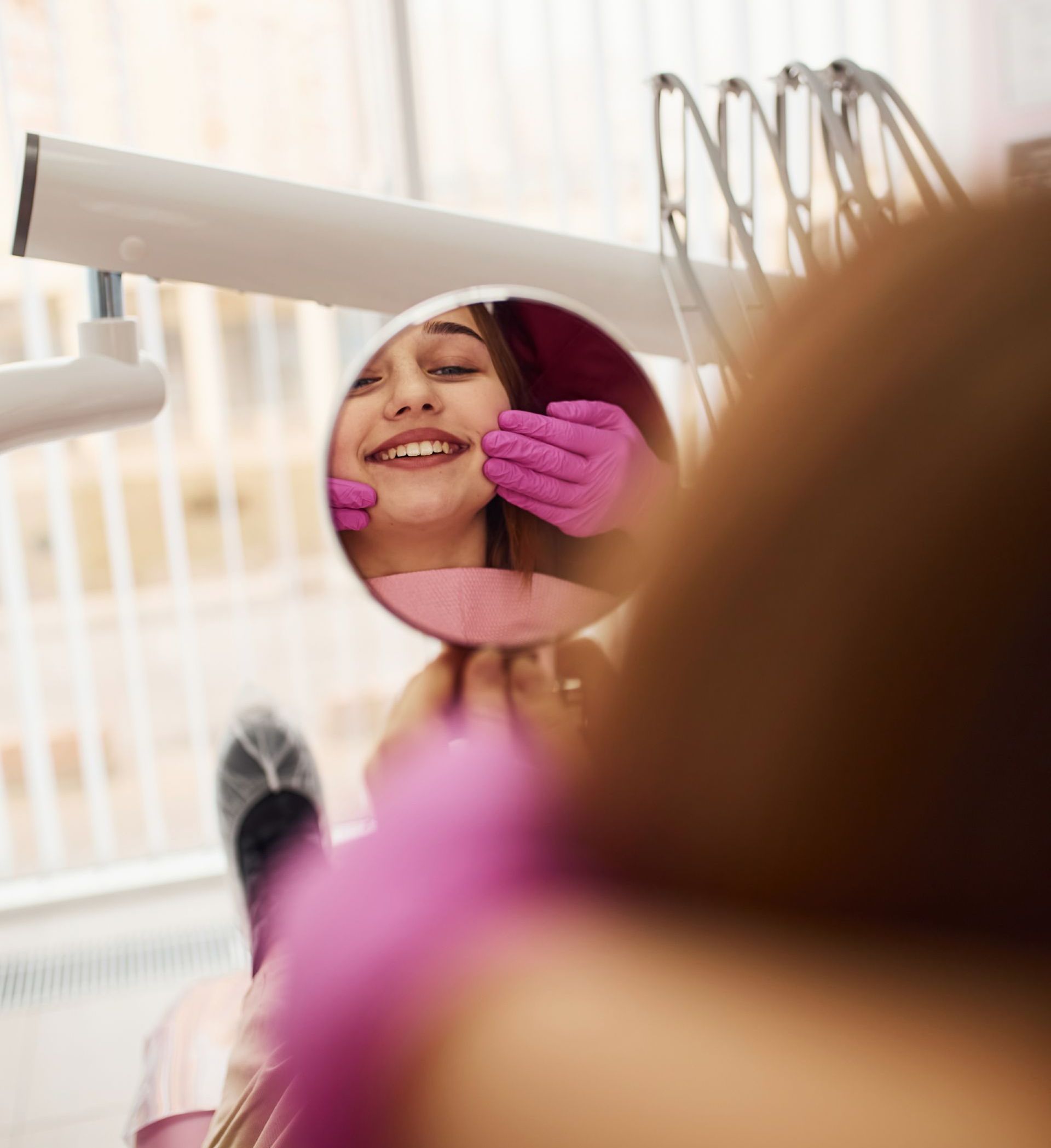 Get cosmetic dental care including veneers, whitening, and Invisalign. woman smiling in mirror at dentist | Cosmetic dentist offers teeth whitening, veneers, Invisalign clear aligners