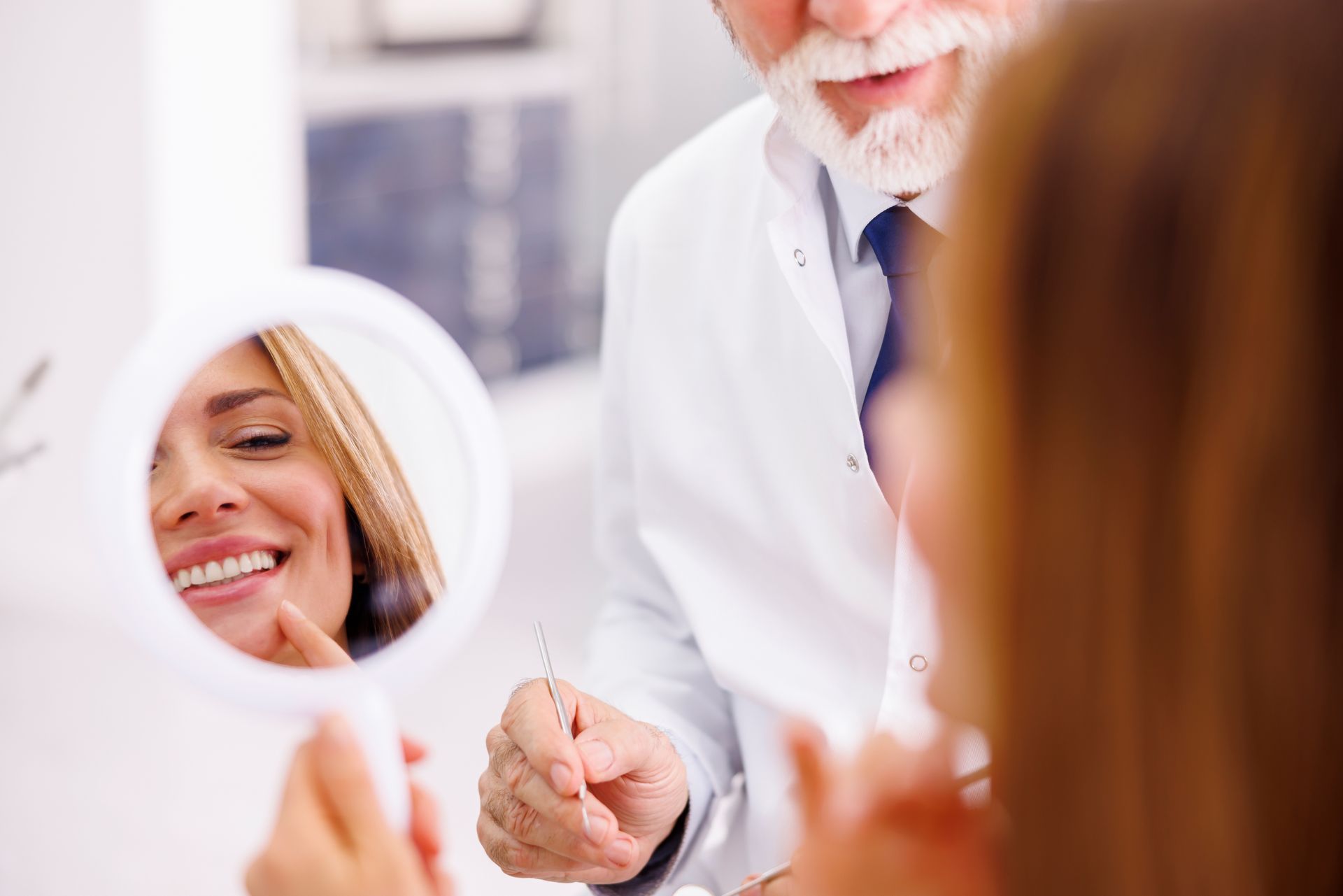 We are Somerset, NJ's top dentist for cosmetic dental care. woman smiling in mirror after teeth whitening and invisalign treatments | Somerset NJ best dentist