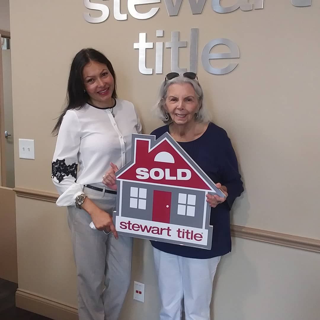 Two women in a Stewart Title office celebrate a home sale. One holds a