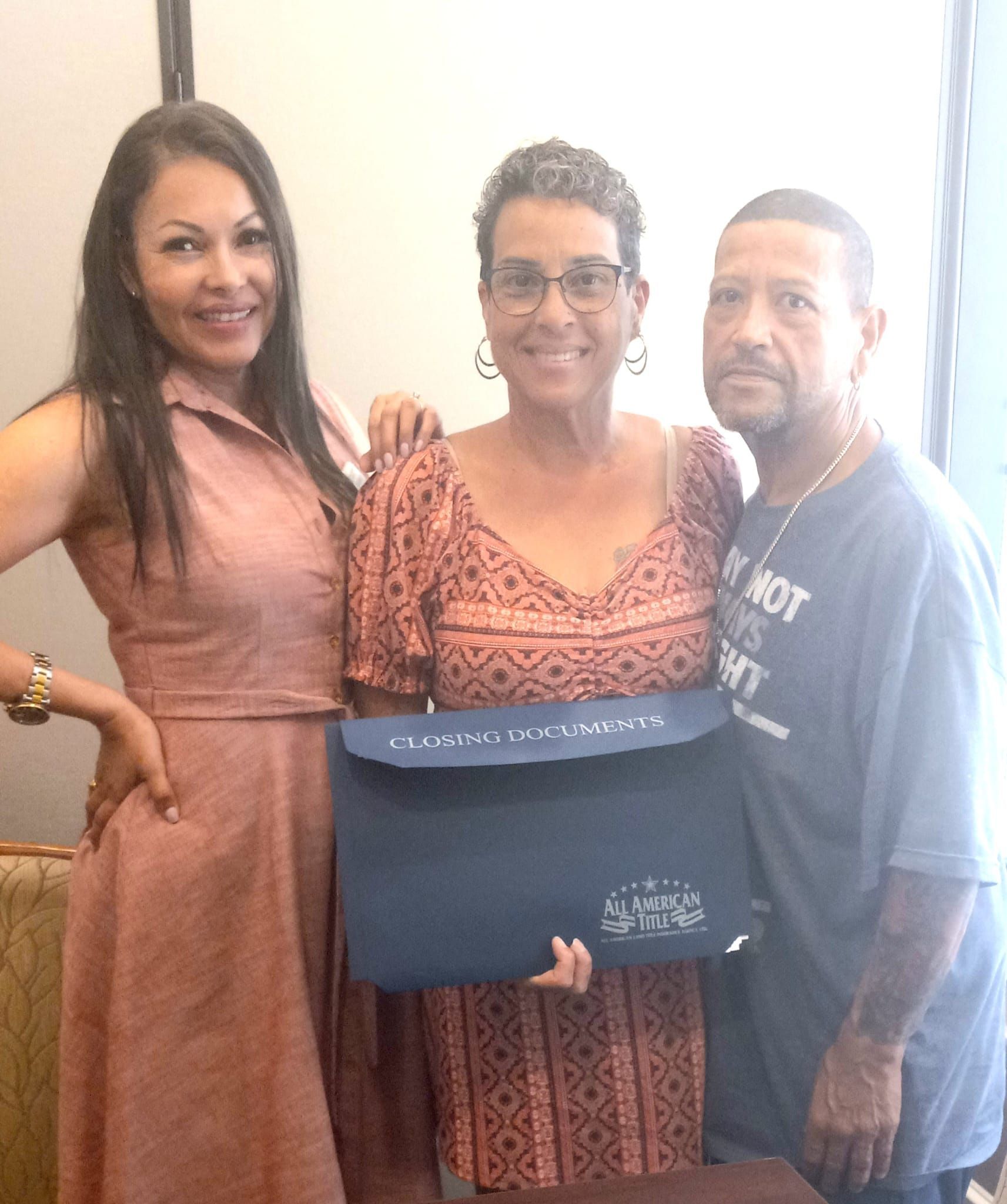 Three people standing and smiling, holding a dark blue document.
