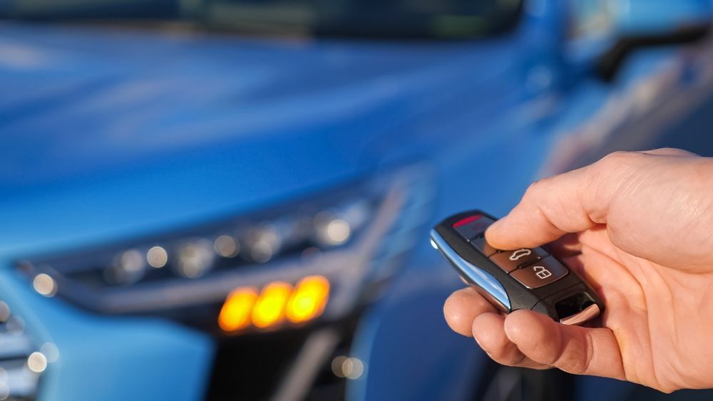 A person is holding a remote control in front of a blue car.