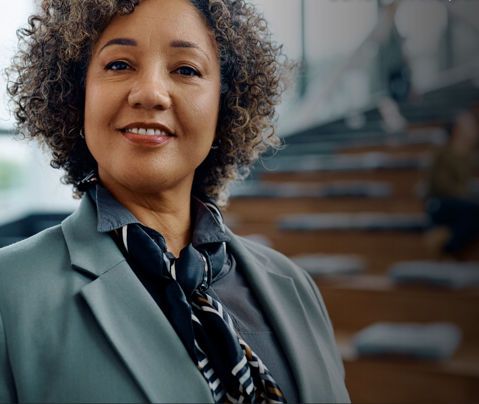 Woman in business suit with arms crossed, smiling, with colleagues in the background.