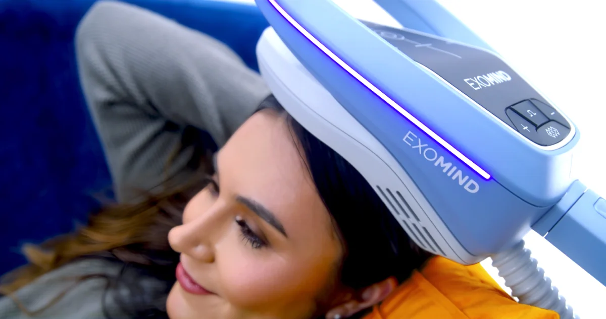 A person relaxing as a blue Exomind device is positioned over their head for a wellness treatment.