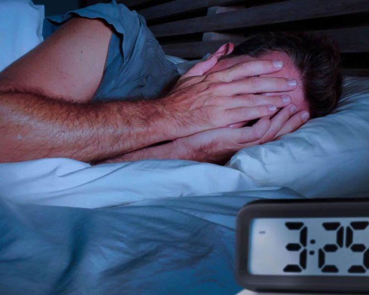 A person lies in bed at night, covering their face with their hands, while a digital clock shows 3:25.