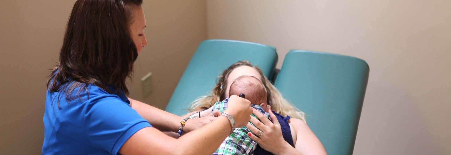 Caregiver holding a baby seated in a teal medical chair during an exam