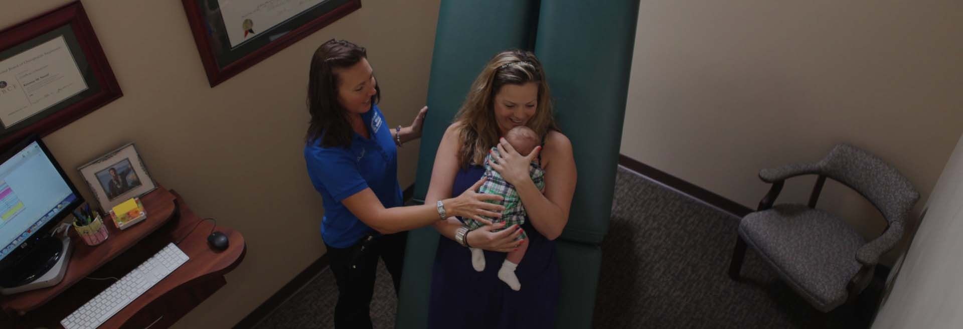 Two women holding a baby in a hallway, with one woman checking the infant's face.