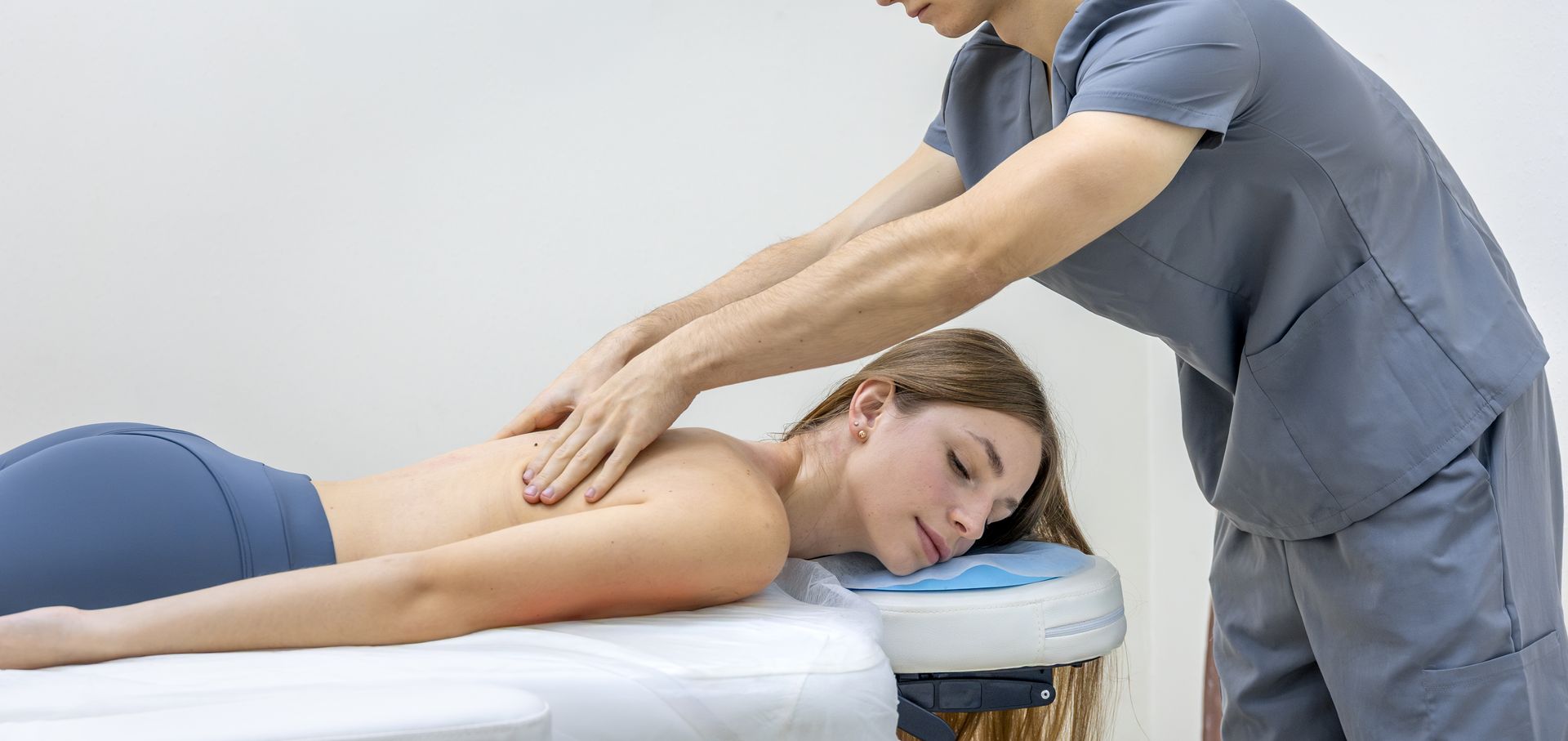 Massage therapist stretching a client’s back on a treatment table in a bright clinic