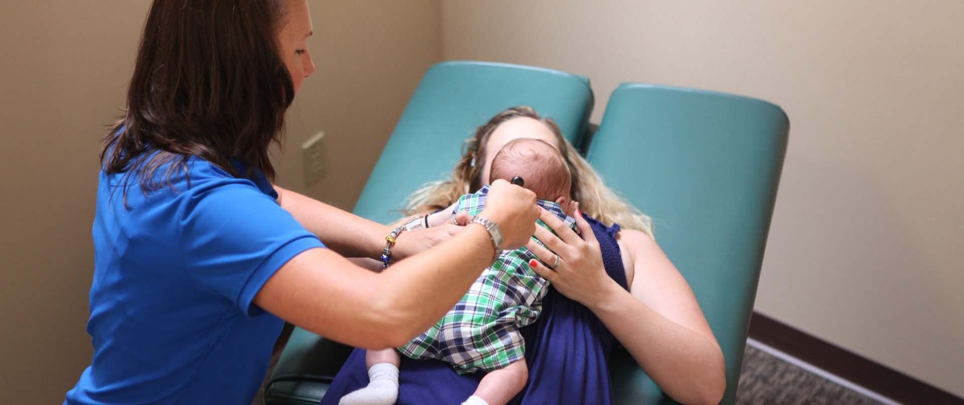 Woman holding a baby in a reclining chair during a medical exam
