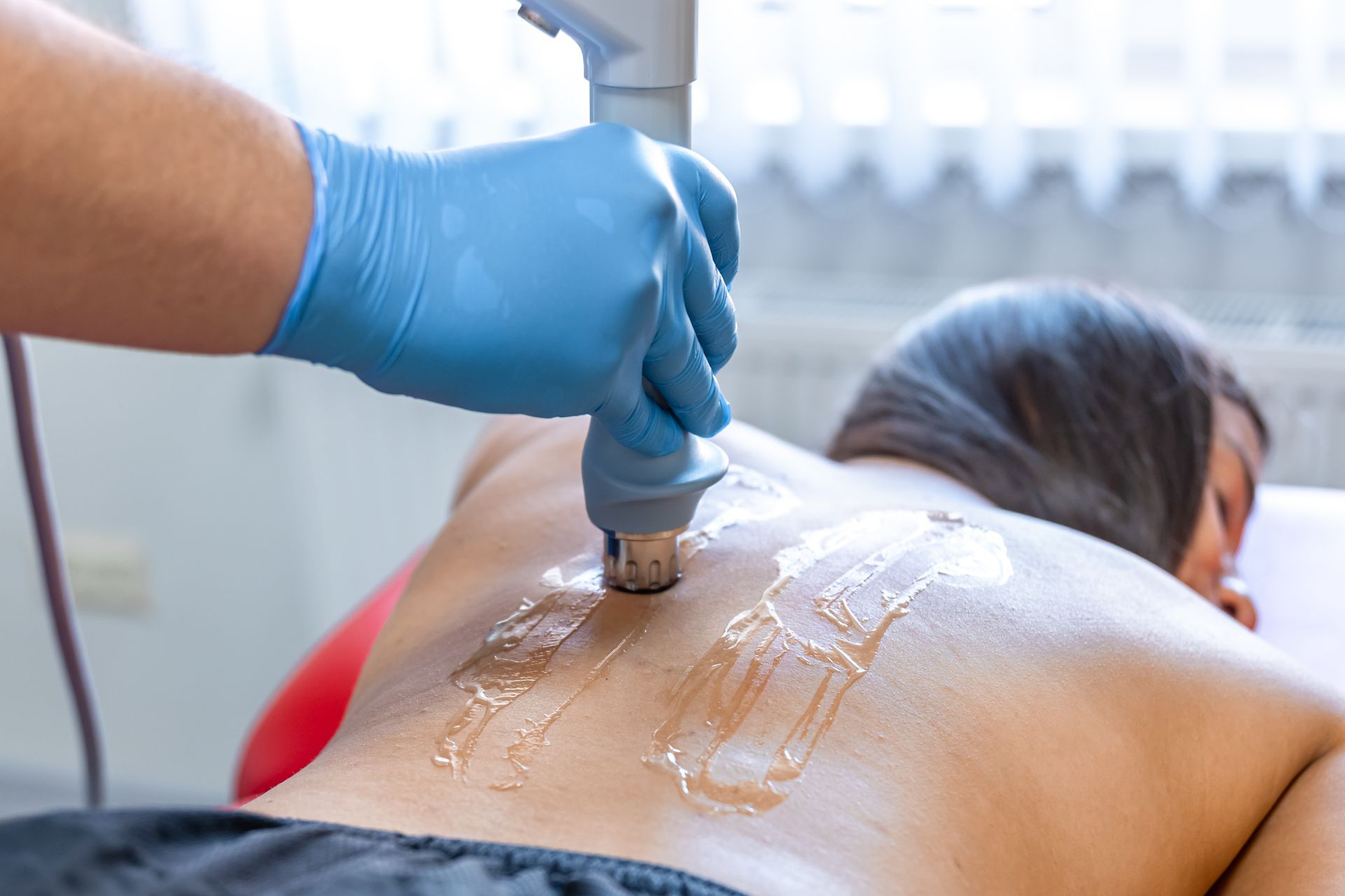 Gloved hand using a red light therapy device on a patient's back