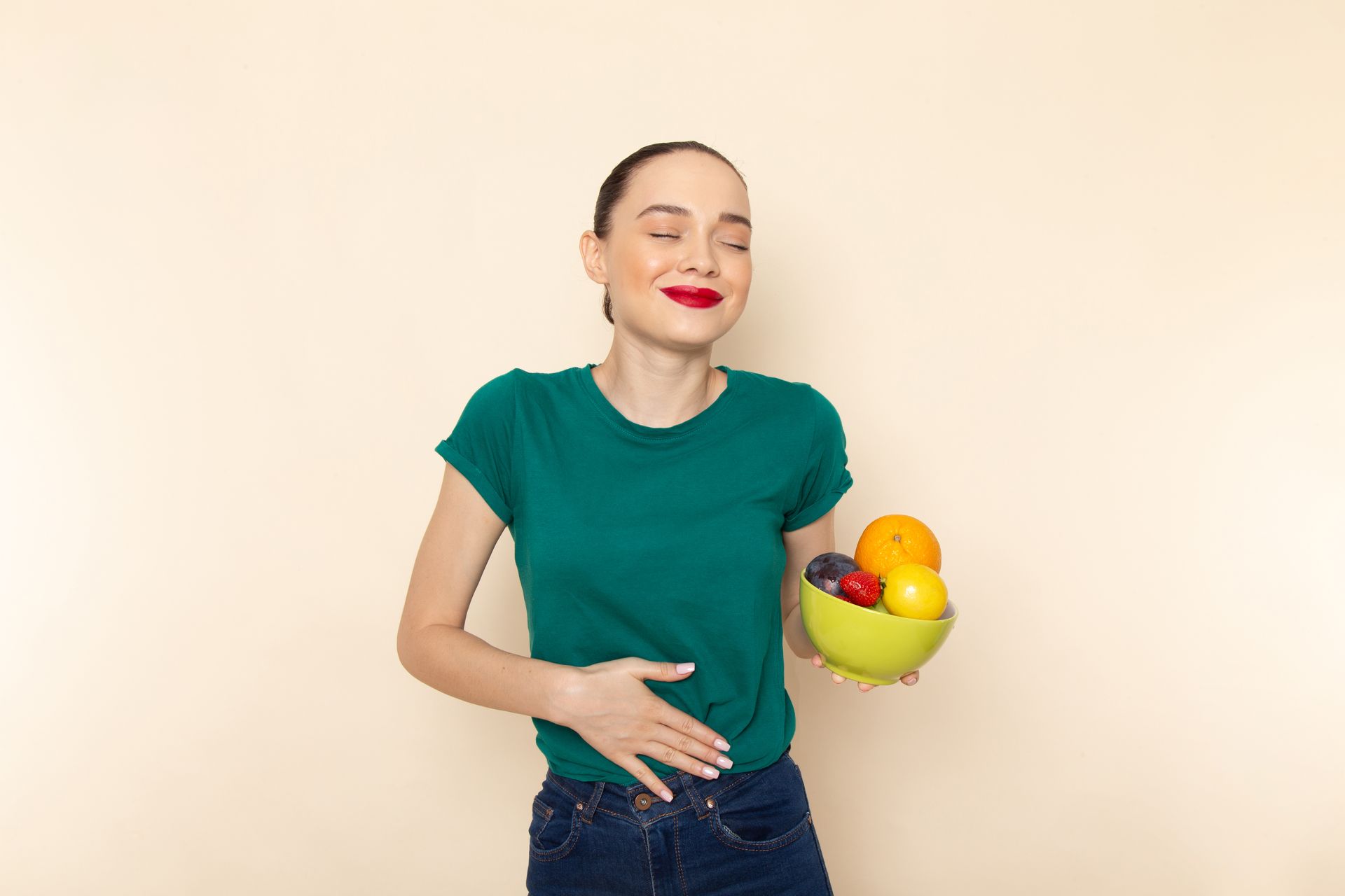 Woman in a green shirt smiling and holding a bowl of fruit against a plain background