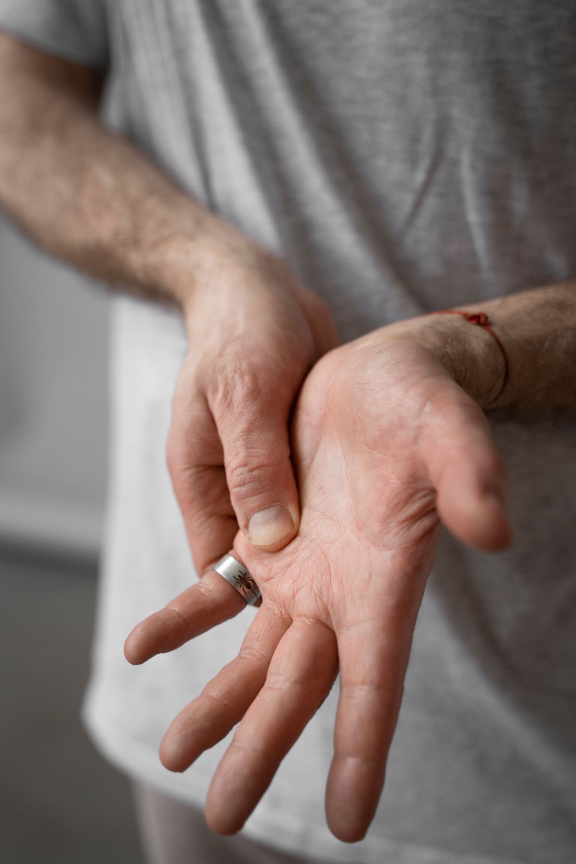Person holding an open palm while touching the wrist with the other hand, wearing a gray shirt.