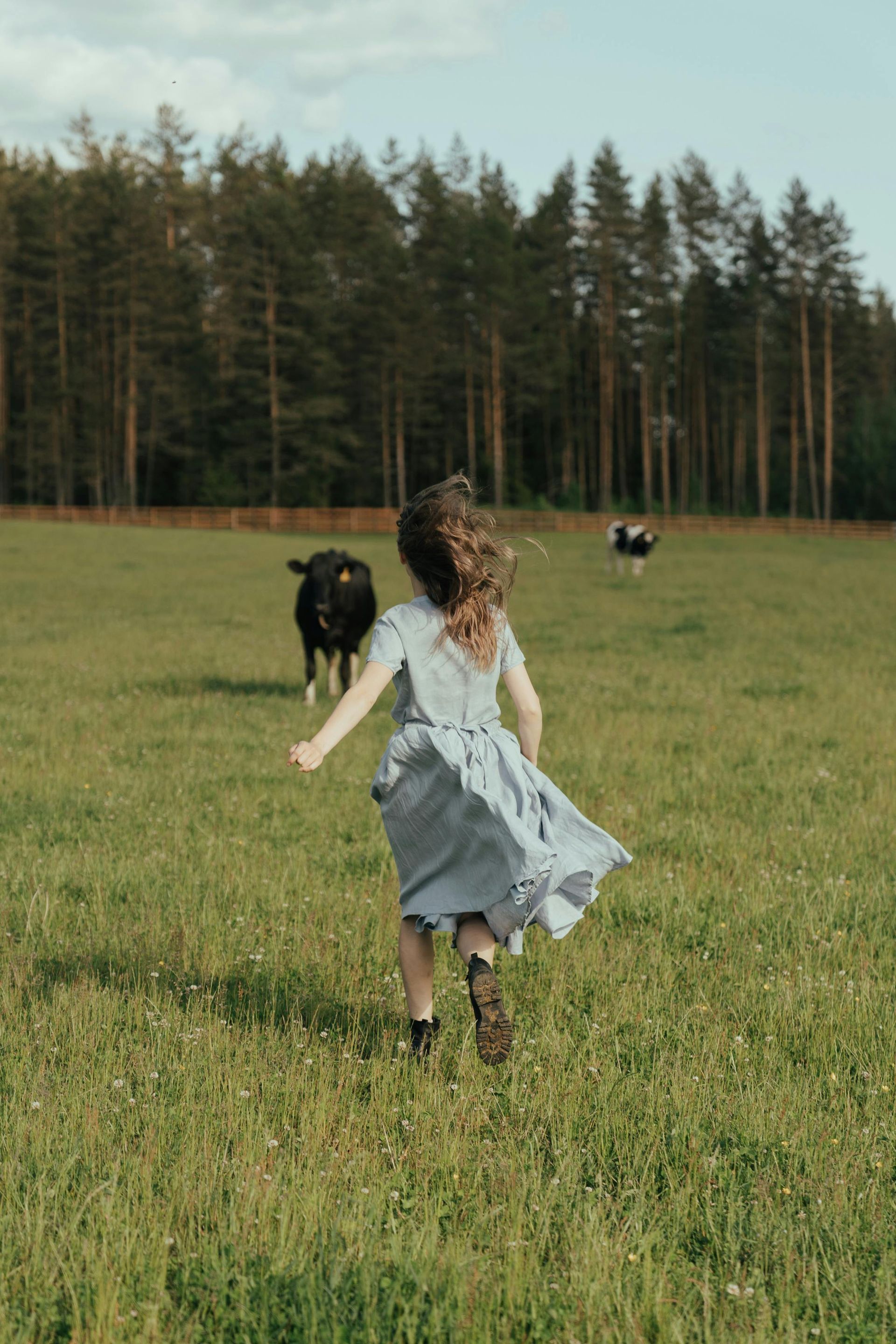 A little girl is running in a field with a cow in the background.
