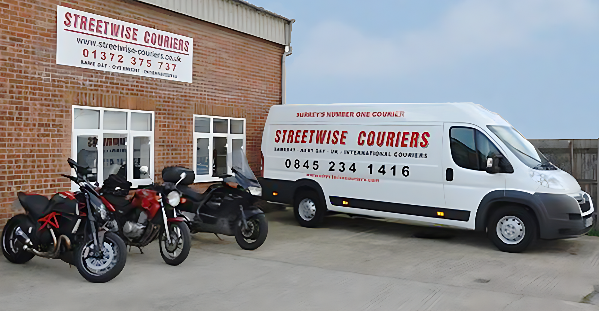 Motorcycles and a white delivery van outside a brick building with a courier sign