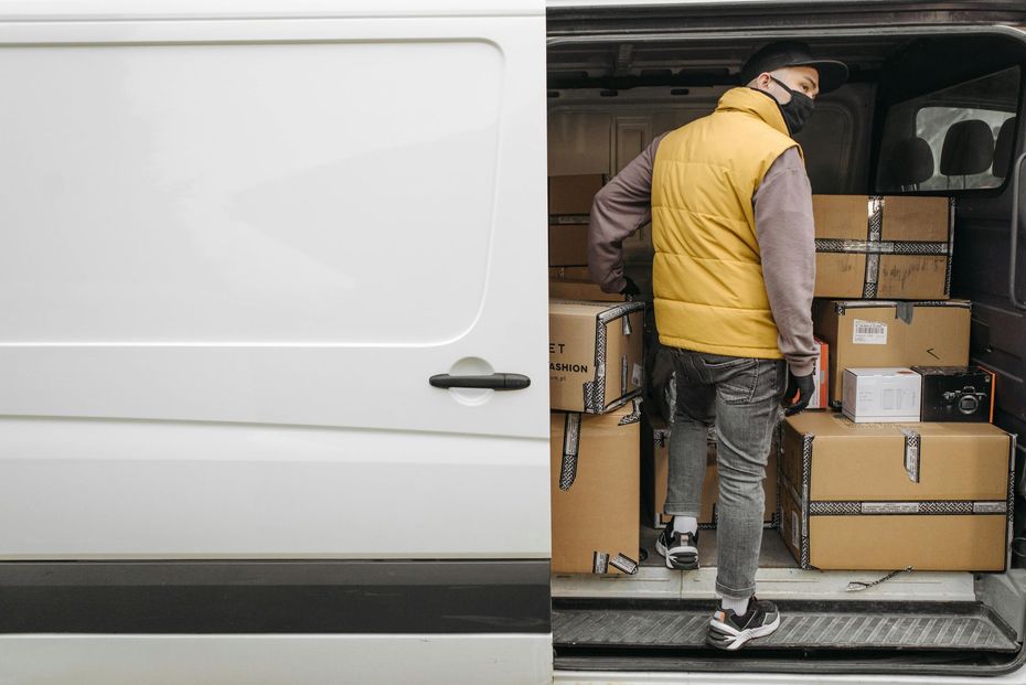 Zed Logistics delivery driver loading cardboard boxes into a white delivery van.