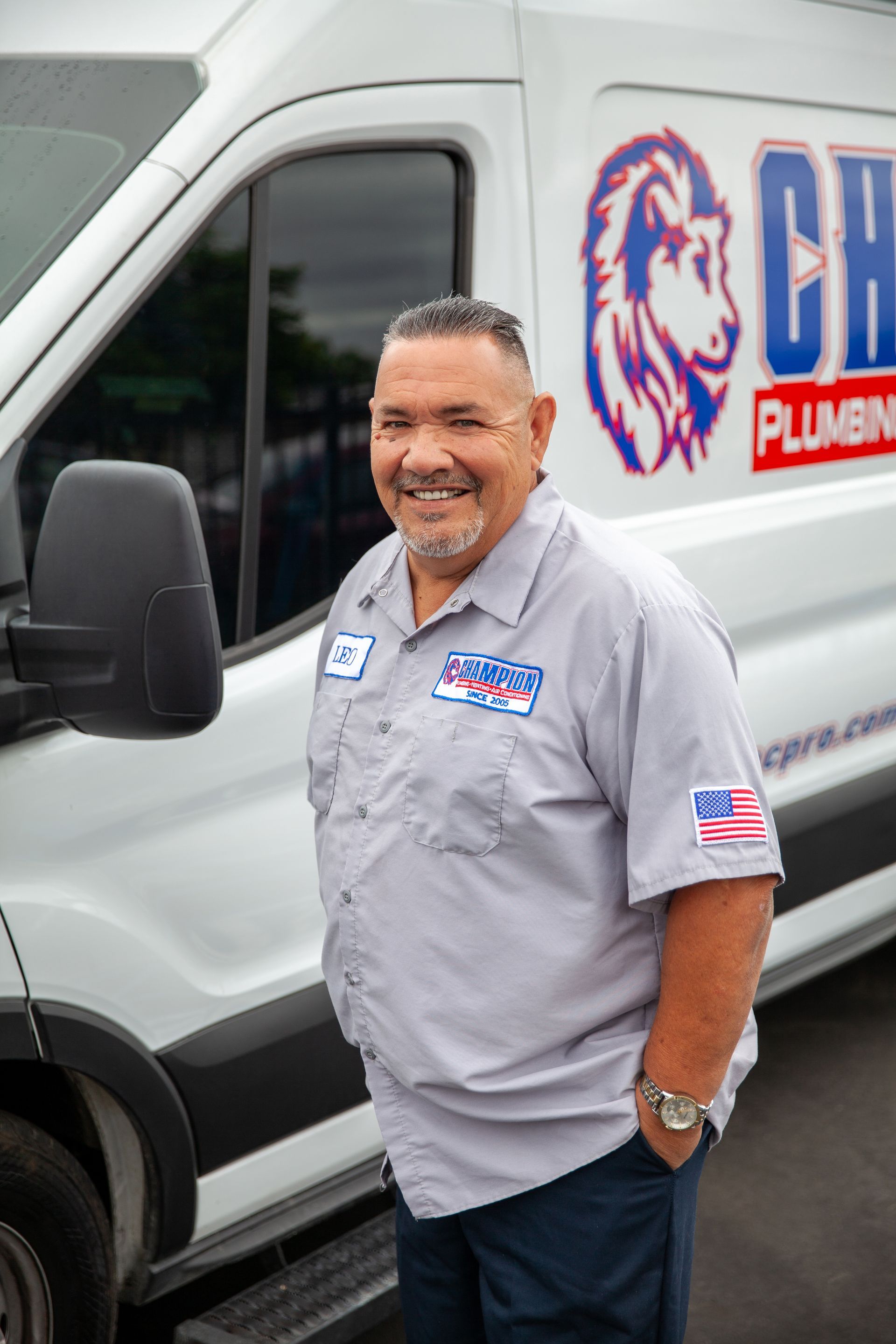 Smiling plumber standing beside a white service van with a plumbing logo.