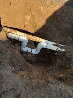 A white pipe is sitting in the dirt next to a rock.