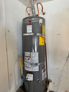 A water heater is sitting in a corner of a room next to a wall.
