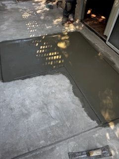 A person is laying concrete on a sidewalk next to a door.
