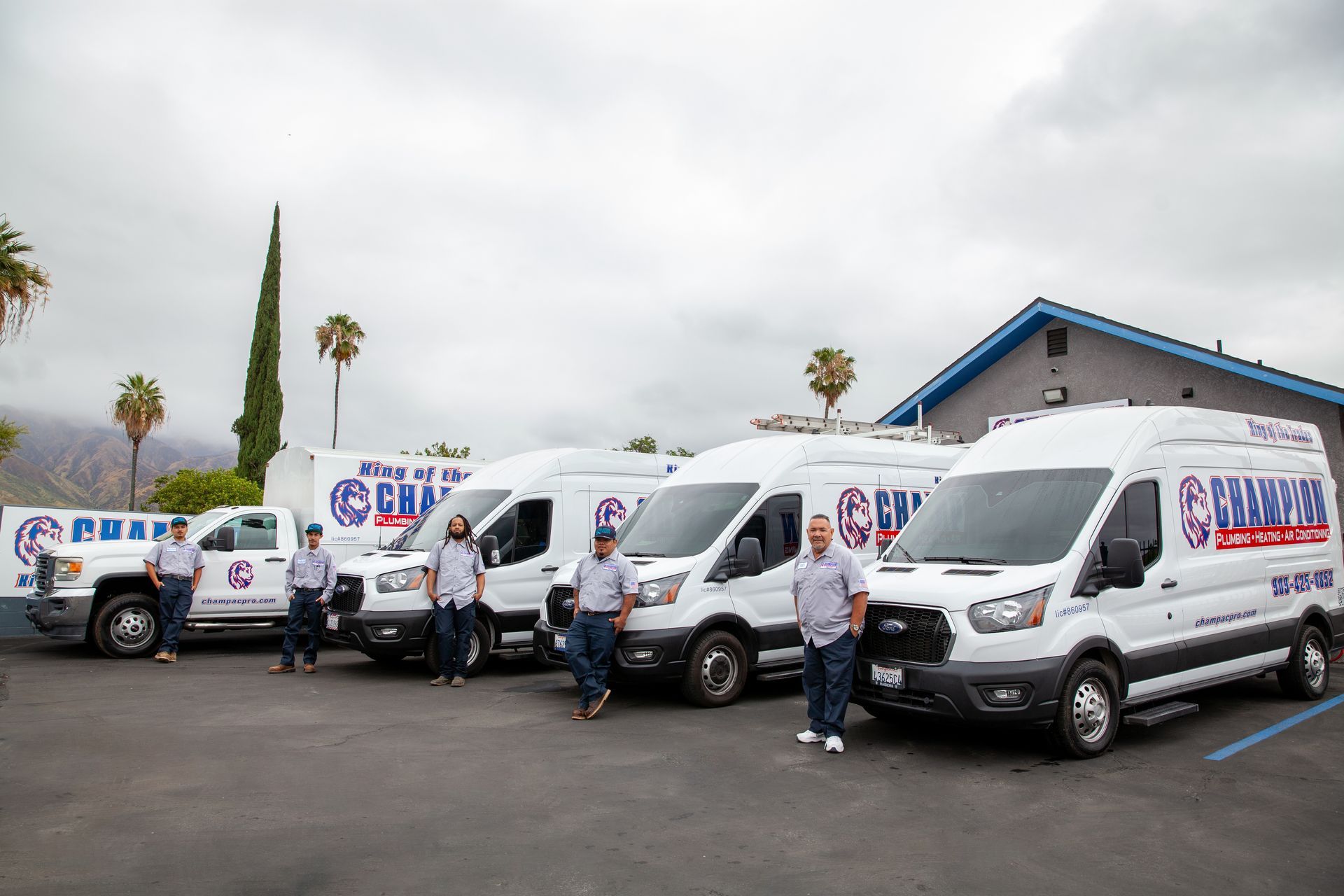 People standing beside a row of white vans in a parking lot under cloudy skies.
