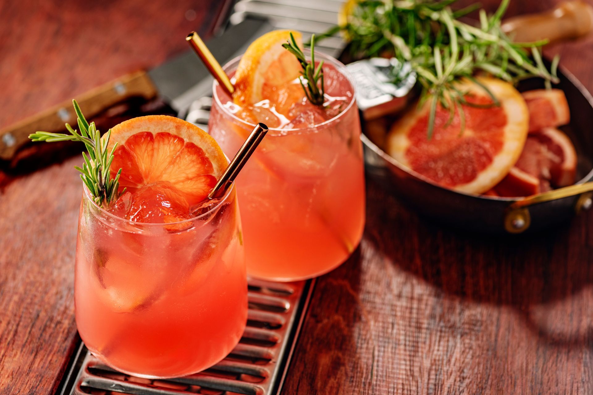 Two grapefruit cocktails garnished with rosemary, on a wooden surface.