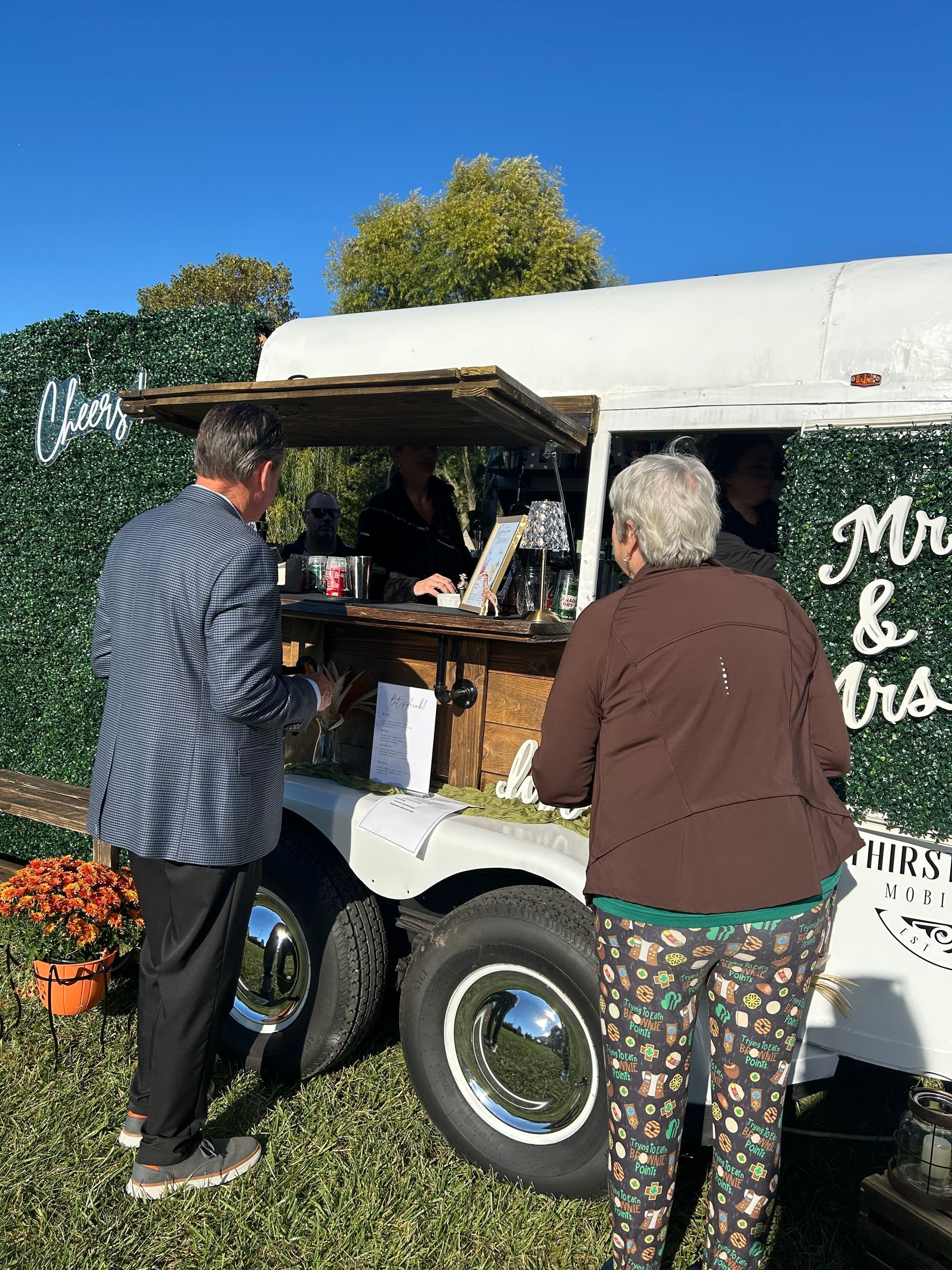 People at a mobile bar with a floral wall. The bar has 