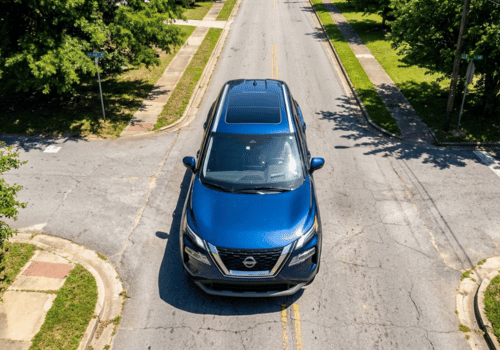 Aerial view of a blue SUV driving through a quiet residential neighborhood with tree-lined streets.