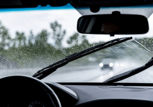 Windshield wipers clearing rain from a car windshield on a wet road with headlights ahead