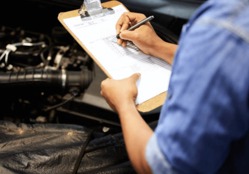 Mechanic writing on a clipboard beside an engine in a workshop