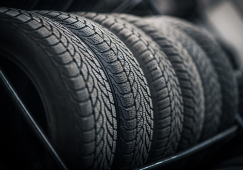 Row of black car tires with deep tread patterns stacked in a dark rack