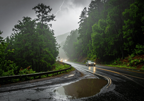 Car driving on a rain-soaked forest road with puddles and lightning
