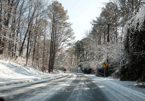 Snow-covered road winding through a winter forest with a yellow curve sign on the right