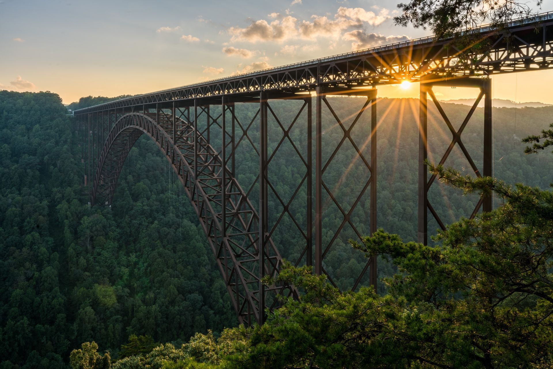 Sunlit steel arch bridge spanning a forested gorge at sunset