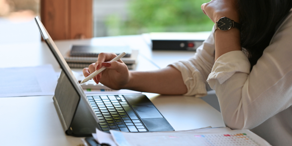 Person working at a desk with a laptop and writing on paper in a bright office.