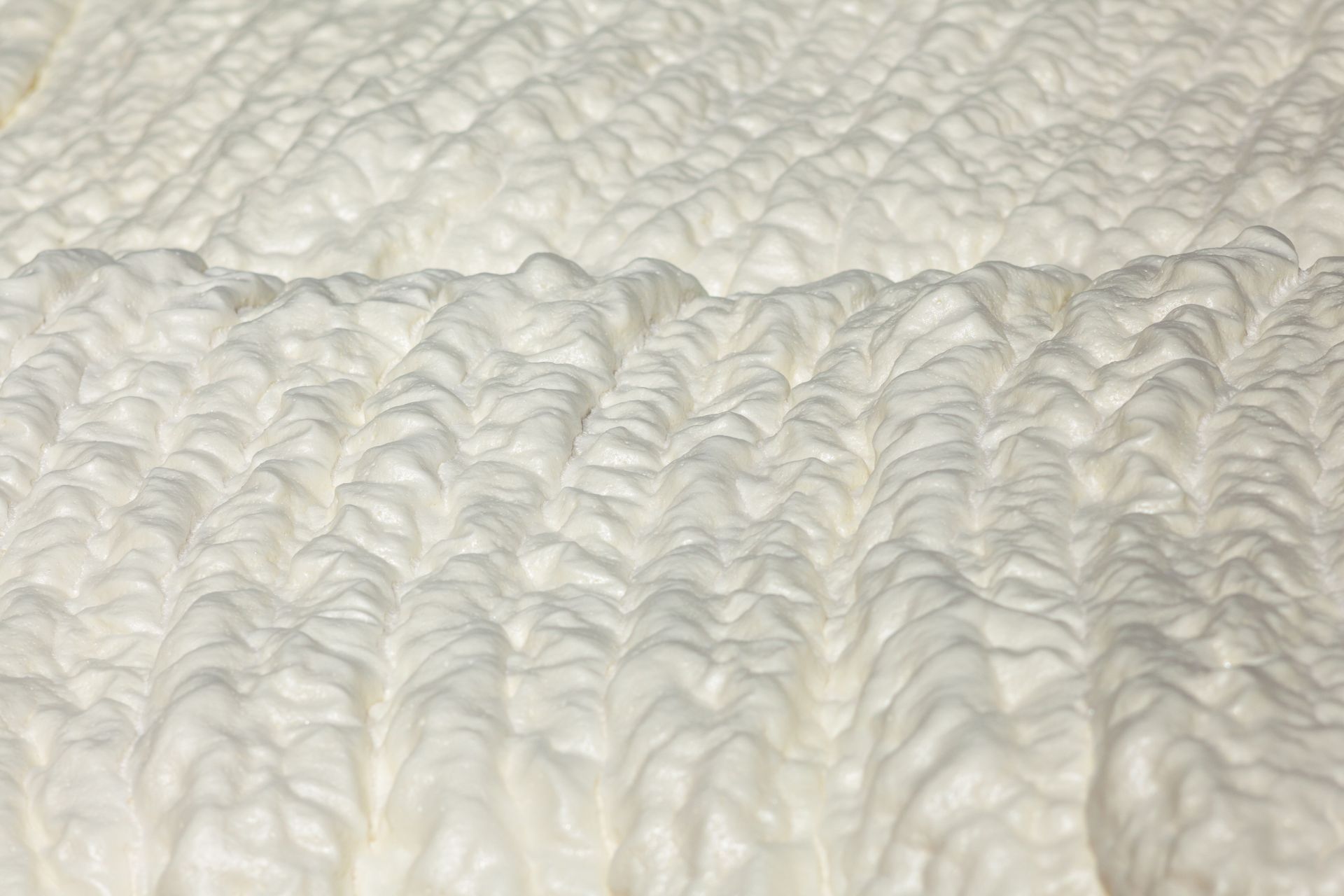 Gros plan d'un tissu texturé blanc avec une surface matelassée et bosselée, montrant un motif de crêtes parallèles.