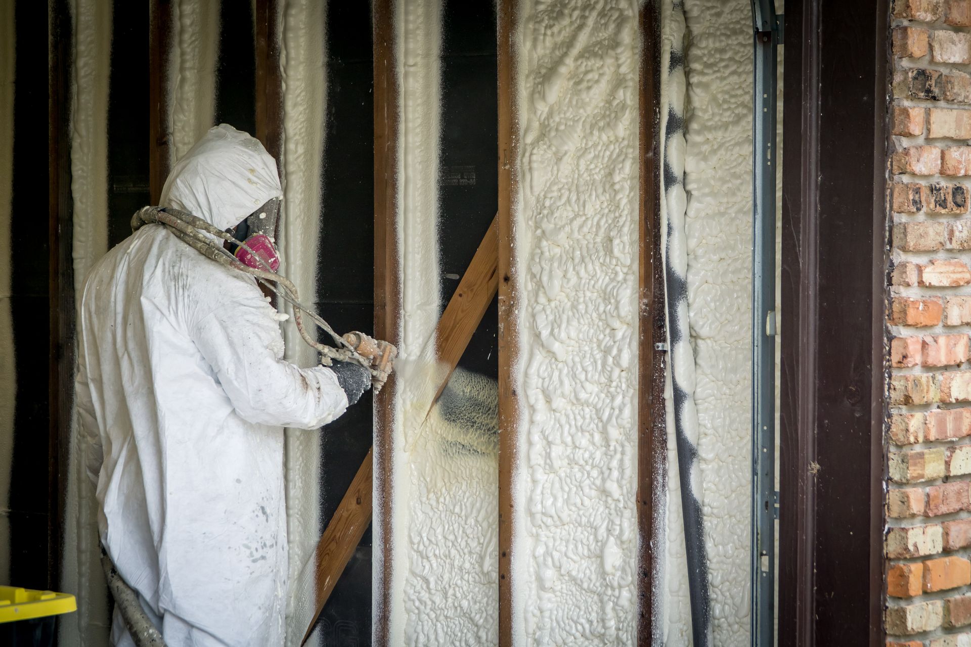Une personne en combinaison de protection pulvérise de l'isolant en mousse sur un mur.