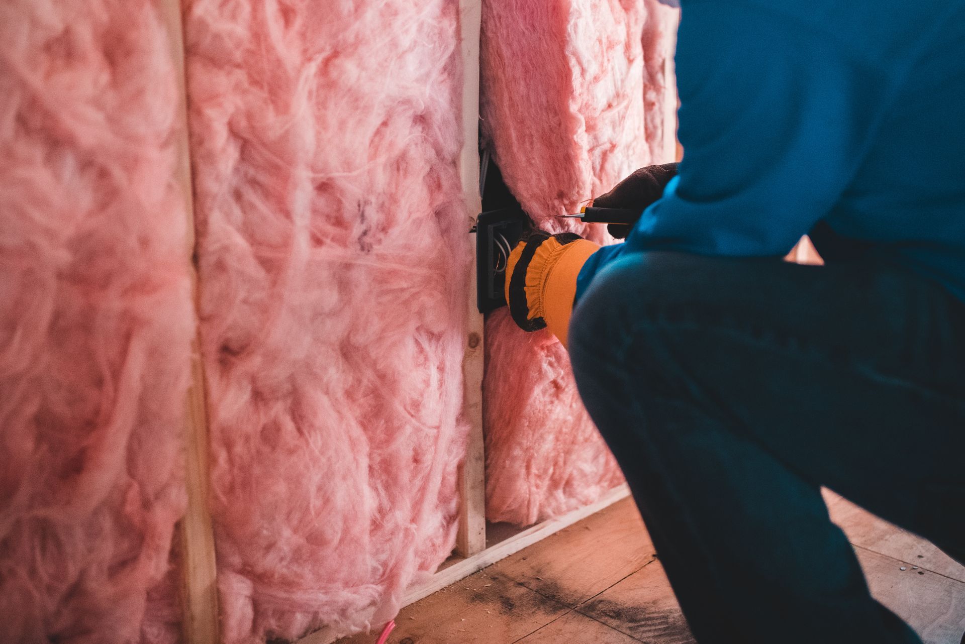 Personne installant de l'isolant rose entre les montants muraux en bois.