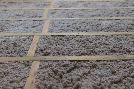 Isolant en cellulose grise entre des bandes de bois, probablement dans un plancher ou un plafond.