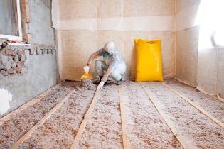 Une personne installe de l'isolant dans une pièce, agenouillée entre des poutres en bois.