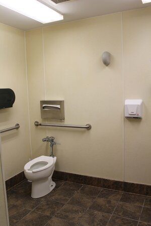 A bathroom with a toilet , handrails , and a paper towel dispenser.
