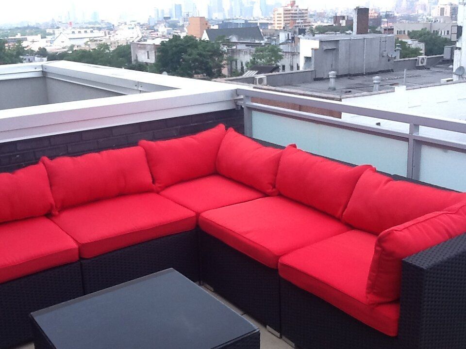 A couch with red cushions sits on a balcony overlooking a city