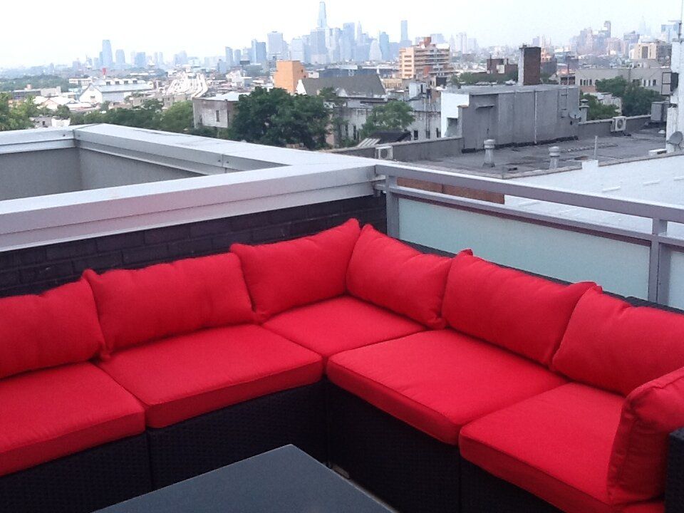 A couch with red cushions sits on a balcony overlooking a city