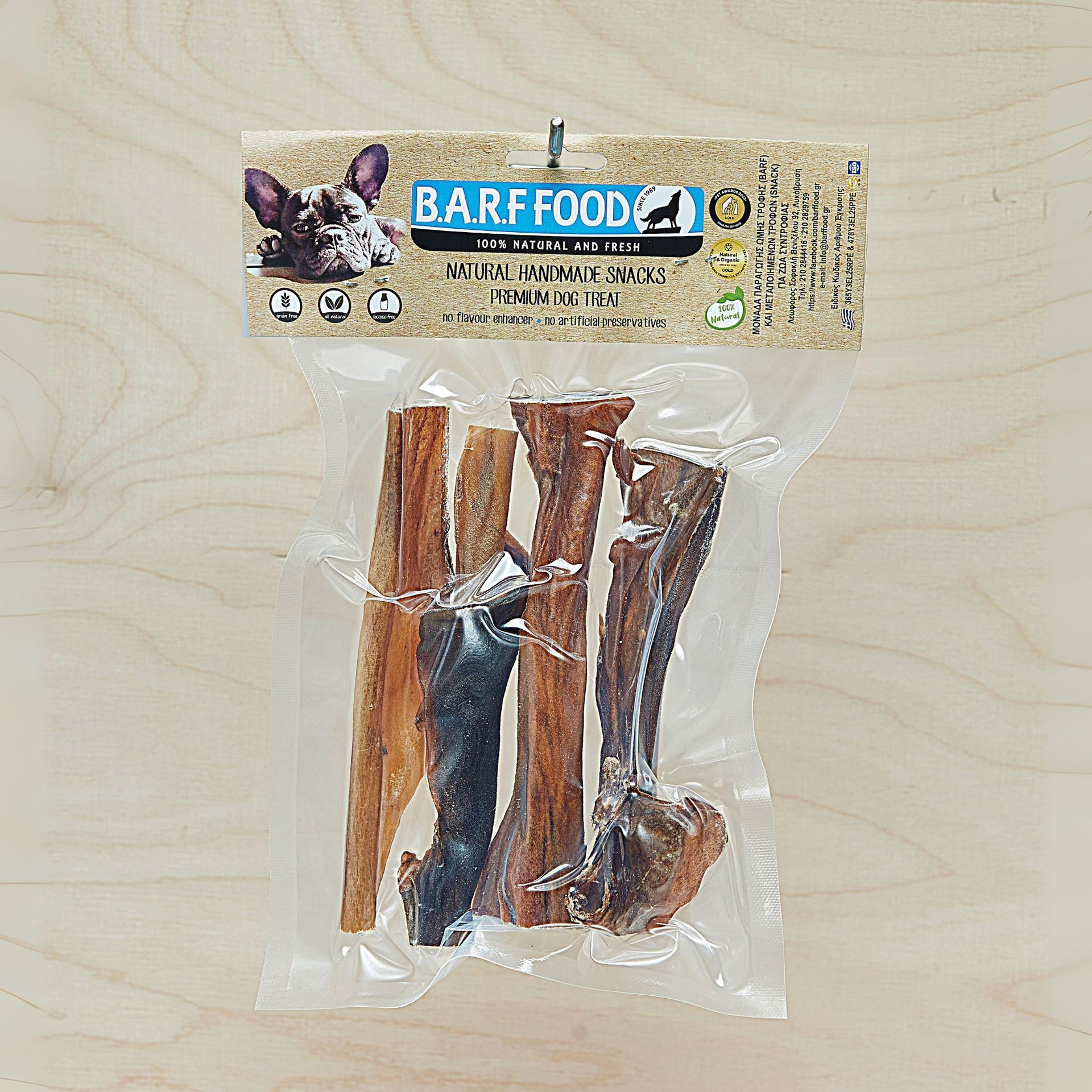Συσκευασία λιχουδιών για σκύλους BARF Food, που περιέχει αρκετές καφέ και καφέ μασώμενες μπάλες, σε ανοιχτόχρωμη ξύλινη επιφάνεια.